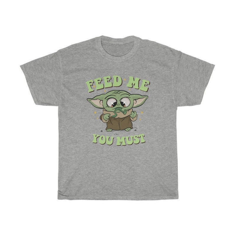 May include: A heather gray t-shirt featuring a cartoon image of a green alien character with large eyes and pointed ears. The text "FEED ME YOU MUST" is printed above and below the character in green lettering.
