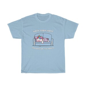 K&ouml;nnte beinhalten: Hellblaues T-Shirt mit einem Cartoon-Einhorn, das auf einem Sofa schl&auml;ft. Der Text "WORK FROM HOME" steht &uuml;ber dem Sofa und "EMPLOYEE OF THE MONTH" darunter. Das Einhorn hat eine bunte M&auml;hne und ist mit einer lila Decke bedeckt.
