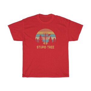 Pode incluir: T-shirt vermelho com um design retro de disc golf. O gr&aacute;fico inclui um cesto de disc golf, um disco e &aacute;rvores contra um p&ocirc;r do sol. O texto "STUPID TREE" est&aacute; abaixo.