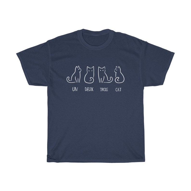 May include: Navy blue t-shirt featuring a white graphic of four stylized cats in different poses. Below the cats, the text reads "UN DEUX TROIS CAT". The shirt is a casual wear item.