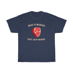Op de afbeelding: Marineblauwe t-shirt met de tekst "MEAT IS MURDER" boven een cartoon steak illustratie. Onder de illustratie staat de tekst "TASTY, TASTY MURDER".