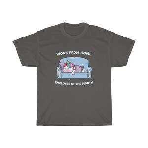 K&ouml;nnte beinhalten: Dunkelgraues T-Shirt mit einem Cartoon-Einhorn, das auf einem blauen Sofa schl&auml;ft. Der Text "WORK FROM HOME" und "EMPLOYEE OF THE MONTH" befinden sich &uuml;ber und unter der Illustration. Das Einhorn hat eine bunte M&auml;hne und ist mit einer lila Decke bedeckt.