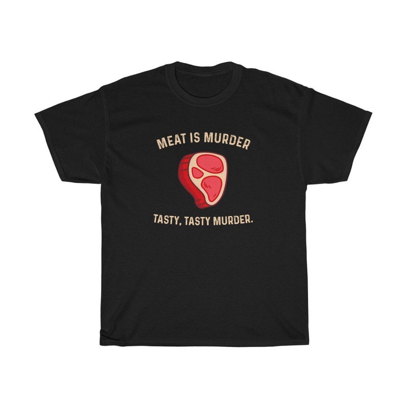 Op de afbeelding: Zwart t-shirt met de tekst "MEAT IS MURDER" boven een cartoon steak illustratie. Onder de illustratie staat de tekst "TASTY, TASTY MURDER."