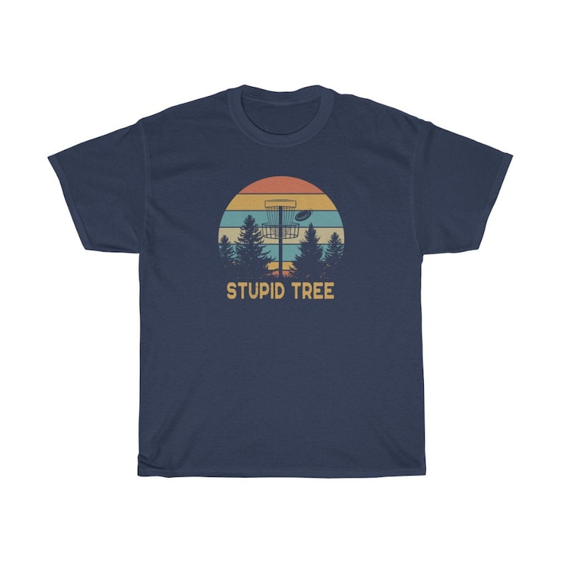 Pode incluir: T-shirt azul marinho com um gr&aacute;fico retr&ocirc; de uma cesta de disc golf, um disco e &aacute;rvores contra um p&ocirc;r do sol. O texto "STUPID TREE" est&aacute; abaixo do gr&aacute;fico. Uma camiseta casual para os entusiastas do disc golf.