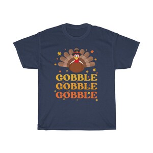 May include: Navy blue t-shirt with a Thanksgiving turkey graphic. The turkey is brown with a red wattle and a pilgrim hat. The words "GOBBLE GOBBLE GOBBLE" are printed in orange and yellow.