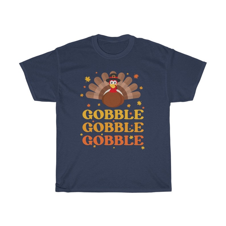 May include: Navy blue t-shirt with a Thanksgiving turkey graphic. The turkey is brown with a red wattle and a pilgrim hat. The words "GOBBLE GOBBLE GOBBLE" are printed in orange and yellow.
