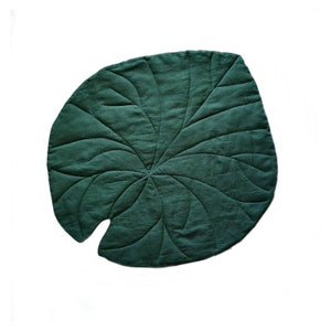Op de afbeelding: Een donkergroene, bladvormige decoratieve mat. De mat heeft een gewatteerd ontwerp met uitstralende lijnen die de nerven van een blad nabootsen. De mat is gemaakt van een zachte, getextureerde stof en staat tegen een witte achtergrond.