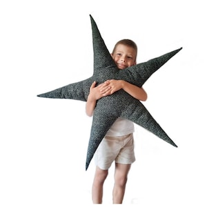 Könnte beinhalten: Ein Kind umarmt ein großes, sternförmiges Kissen in Schwarz und Weiß. Das Kissen ist aus weichem Stoff und hat ein verspieltes Design.