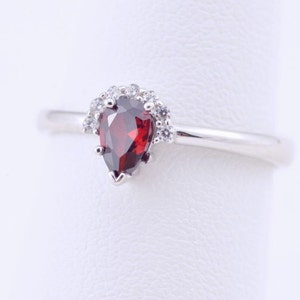 May include: A silver ring with a pear-shaped red gemstone surrounded by smaller white gemstones.