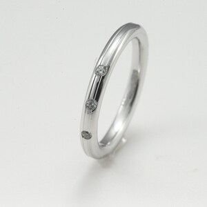 May include: A simple silver band ring with three small diamonds set into the band.