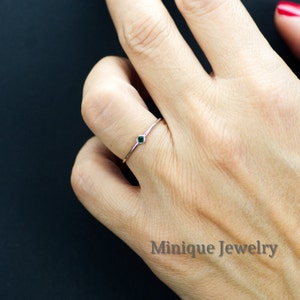 May include: A delicate silver ring with a small, dark green gemstone. The ring is worn on a finger.