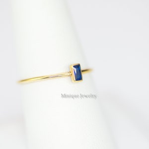 May include: A delicate gold ring featuring a rectangular, deep blue gemstone. The ring has a thin band and a minimalist design, perfect for everyday wear. The ring is shown on a white background.