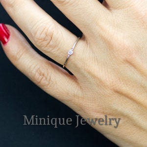 Könnte beinhalten: Ein zarter Silberring mit einem einzigen, kleinen, klaren Edelstein. Der Ring wird an einem Finger getragen.