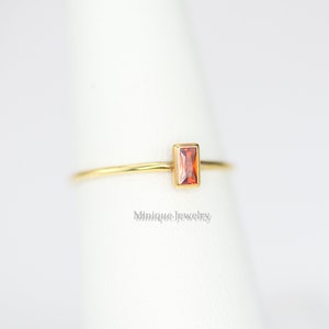 May include: A gold ring with a small, rectangular, orange gemstone.