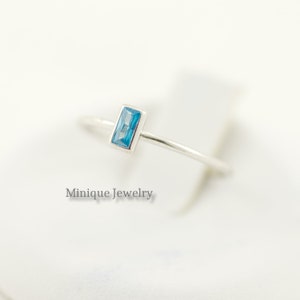 May include: A silver ring with a light blue rectangular gemstone. The ring is on a white background. Minique Jewelry.
