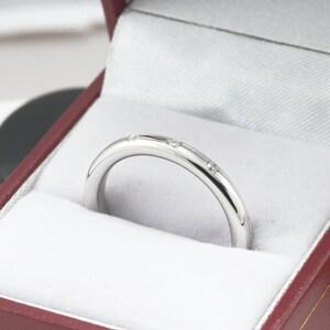 May include: A thin silver band with small diamonds set into the metal. The ring is in a red velvet box.