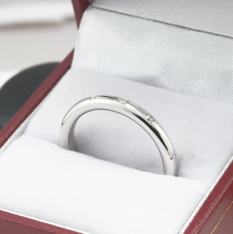 May include: A thin silver band with small diamonds set into the metal. The ring is in a red velvet box.