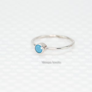 May include: A delicate silver ring with a small, round, light blue gemstone.