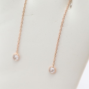 May include: A pair of rose gold dangle earrings with small clear stones at the end of each chain.