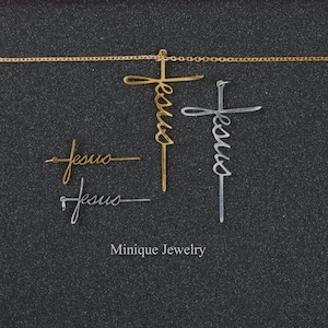 May include: Two gold and silver necklaces with the word "Jesus" written in cursive on each cross pendant. The necklaces are on a black background. The text "Minique Jewelry" is written below the necklaces.