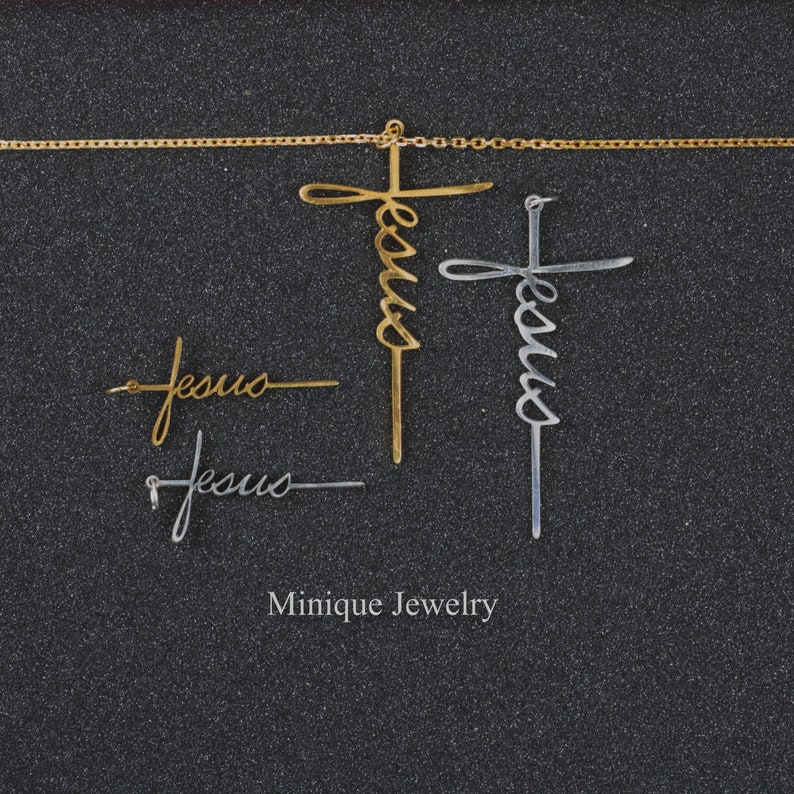 May include: Two gold and silver necklaces with the word "Jesus" written in cursive on each cross pendant. The necklaces are on a black background. The text "Minique Jewelry" is written below the necklaces.
