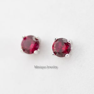 May include: A pair of silver stud earrings with a round, red gemstone in the center of each earring.