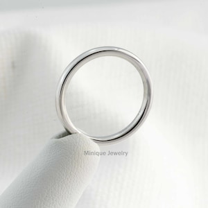 May include: A simple, silver wedding band with a smooth, polished finish. The band is shown on a white display stand.
