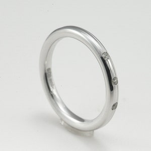 May include: A silver band ring with three small diamonds set into the band.