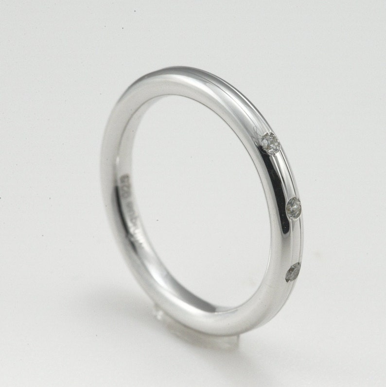 May include: A silver band ring with three small diamonds set into the band.
