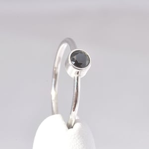 May include: A silver ring with a black gemstone set in a bezel setting.