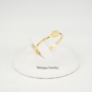 May include: A delicate gold ring with a small square-shaped setting adorned with tiny clear cubic zirconia stones.