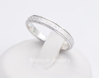 May include: A silver ring with a textured band of small, sparkling stones. The ring is displayed on a white stand against a white background. The text "Minique Jewelry" is visible on the stand.