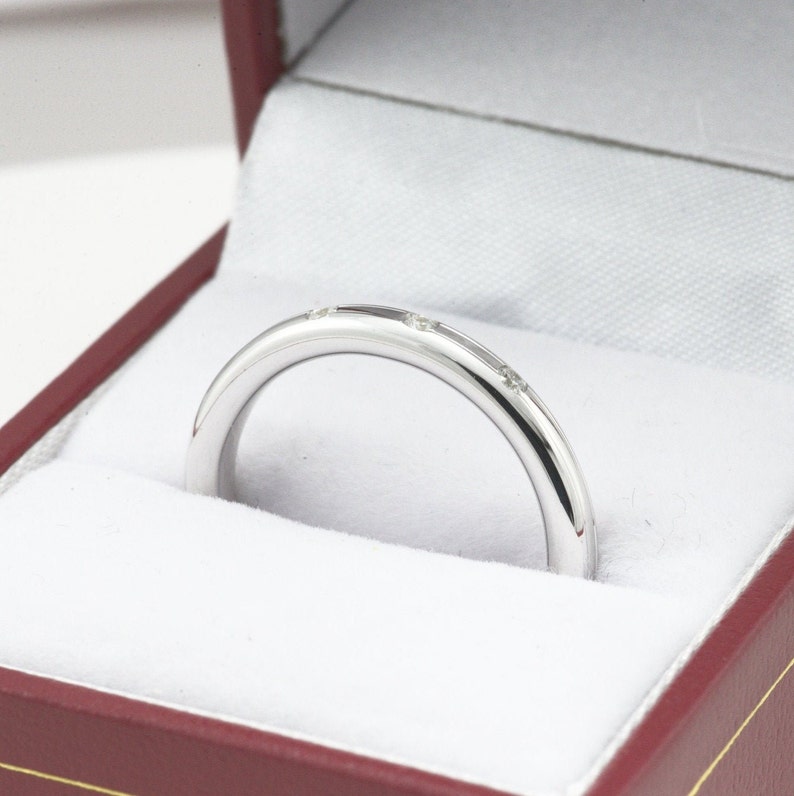 May include: A thin silver band with small diamonds set into the metal. The ring is in a red velvet box.