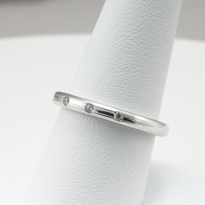May include: A thin silver band with three small diamonds set into the metal.