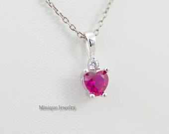 May include: A silver necklace with a heart-shaped pendant featuring a pink gemstone and a smaller clear gemstone. The pendant is set in a silver setting with a delicate chain.