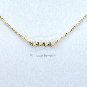 May include: A gold chain necklace with a delicate cursive 'nana' pendant. The necklace is on a white background.