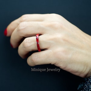 May include: A thin red ring with a marbled pattern. The ring is worn on a person's finger.