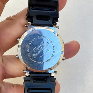 May include: A black Casio digital watch with a silver-tone back. The watch has a black strap and the text "Shock Resistant" and "Water Resistant 200M". The model number is 240DW-5200.