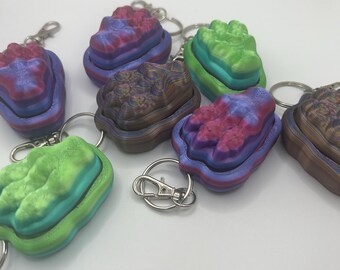 Peut inclure: Un ensemble de six porte-clés colorés, superposés, imprimés en 3D. Chaque porte-clés présente une combinaison de couleurs différente et un design unique. Les porte-clés sont en plastique lisse et brillant.