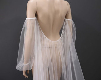 May include: A white tulle bridal cape with long sleeves and a low back. The cape is sheer and has a flowing silhouette. The text "KIM ALPHA BRIDAL" is visible in the upper right corner of the image.