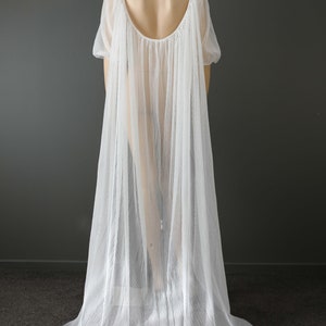 May include: A white, pleated bridal cape with a flowing design. The cape features a scoop back and short sleeves. The Kim Alpha Bridal logo is visible in the upper left corner.