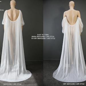 May include: A white bridal cape with a flowing design, shown in two styles: shoulder cape and off-shoulder cape. The cape features long sleeves and a pleated skirt. Text on the image reads "EASY TO TURN FROM SHOULDER CAPE STYLE TO OFF SHOULDER CAPE STYLE."
