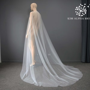 Può includere: Una cappa da sposa in tulle bianco con un lungo strascico. La cappa è drappeggiata su un manichino ed è mostrata da dietro.