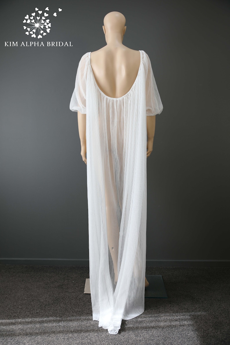 May include: A white, floor-length gown with a pleated design and short sleeves. The gown has a low back and is displayed on a mannequin. The brand name "KIM ALPHA BRIDAL" is visible in the upper left corner.