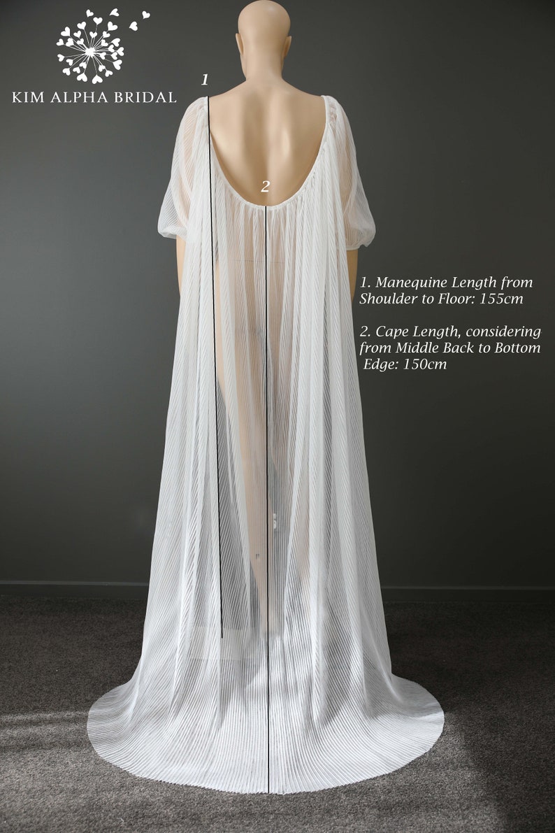 May include: A white, pleated bridal cape on a mannequin. The cape has short sleeves and a low back. The mannequin length from shoulder to floor is 155cm, and the cape length is 150cm. The Kim Alpha Bridal logo is visible.