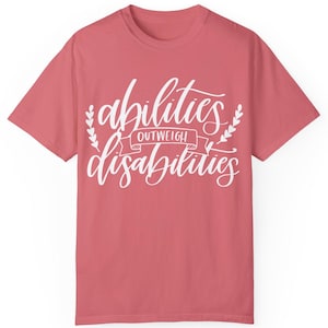 May include: A pink t-shirt with the text "abilities outweigh disabilities" in white lettering.