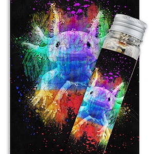 May include: A colorful jigsaw puzzle featuring an axolotl, a type of salamander, with a vibrant rainbow paint splatter effect. The puzzle is packaged in a clear plastic tube with a silver lid.
