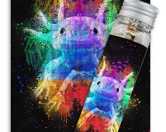 Könnte beinhalten: Ein farbenfrohes Puzzle mit einem Axolotl, einer Salamanderart, mit einem lebendigen Regenbogen-Farbklecks-Effekt. Das Puzzle ist in einem durchsichtigen Plastikrohr mit einem silbernen Deckel verpackt.