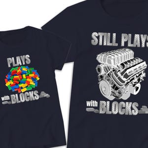 May include: Two navy blue t-shirts. The smaller shirt features a pile of colorful plastic building blocks with the text "PLAYS with BLOCKS". The larger shirt features a detailed engine illustration with the text "STILL PLAYS with BLOCKS".
