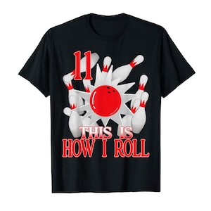 May include: A black short-sleeved t-shirt featuring a graphic of a red bowling ball hitting white bowling pins with red accents. The number 11 is printed in red above the graphic, and the text THIS IS HOW I ROLL is printed in red below.